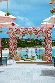 Indian outdoor wedding on platform; pergola decorated with flowers above chairs with white loose covers for bride and groom in front of sea coast