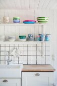 Crockery on bracket shelves above kitchen counter and white-tiled splashback