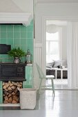 Cast iron kitchen stove with firewood store below in green-tiled cooking area next to open doorway with view into living room