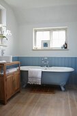 Free-standing, pale blue bathtub against matching, vintage-style blue wainscoting