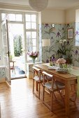 Dining room with pastel floral wallpaper, solid-wood dining table and view into vintage-style conservatory