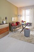 Stilvoller reduzierter Wohnbereich mit pastellgrüner Wand, gemütlicher Lederpolsterbank, rundem Tisch und grauem Polsterhocker