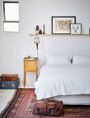 Bedside cabinet next to double bed with white bed linen in simple bedroom