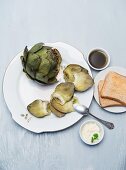 Cooked artichokes on a porcelain plate with aioli and vinaigrette