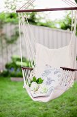 weiße Hortensienblüten und florales Kissen in Hängestuhl im Garten