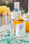 Gin Tonic mit dekorativer Orangenschale und Wacholderbeeren