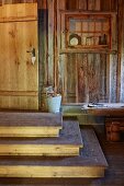 Steps leading up to door in rustic wooden house and old lattice window used as display case on wall