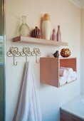 Towel hanging from hook next to rolled towels in shelf module below collection of vases on floating shelf