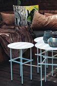 Nest of side tables with white tops in front of comfortable bench with many cushions