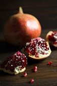 A whole and a broken pomegranate on a dark surface