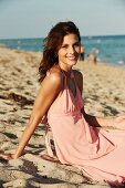 A young woman on a beach wearing a pink summer dress