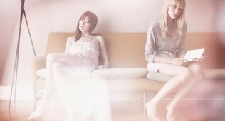 Zwei junge Frauen in heller Kleidung sitzen auf Sofa