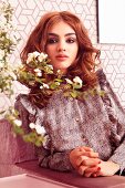 A young woman wearing a patterned ruffled blouse and a flowering sprig of flowers