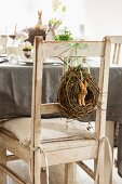 Hare figurine in wicker wreath hung on backrest of chair at table set for Easter celebration