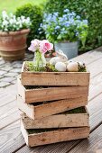 Pink posy in glass vase and Easter decorations in stacked wooden crates on wooden terrace