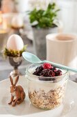 Muesli and berries in screw-top jar with spoon and hare ornament on plate