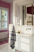 Pattern of light and shade on washstand with white base unit and wall-mounted tap below mirror in niche