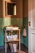 Sink on wooden frame against dado with turquoise and gold patterned wallpaper below gilt-framed mirror on brown-painted wall