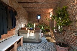 Foyer with brick walls, cobbled floor, coat rack and bench with pale seat cushion