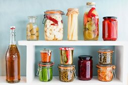 Various preserving jars with vegetables on a shelf with a bottle of home-brewed beer