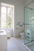 Bad in Weiß, Waschtisch mit integriertem Becken im Unterschrank, gegenüber Duschkabine aus Glas, weiße Mosaikfliesen auf Boden