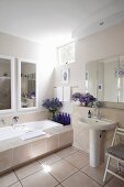 Bathtub with wide tiled surround, large mirror, blue bottles and bouquets