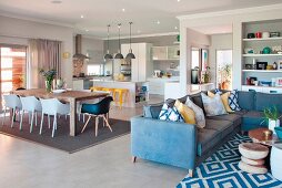 Blue corner sofa with scatter cushions and patterned rug in front of dining area with shell chairs and open-plan kitchen