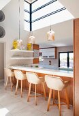 Bar stools with shell seats at white kitchen counter below pendant lamps and large, high windows