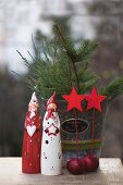 Christmas figurines, red apples and star decorations in front of fir branches in metal bucket