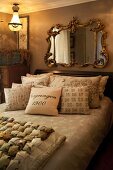 Nostalgisches Schlafzimmer mit Kissensammlung auf französischem Bett, an Wand Spiegel mit verziertem Goldrahmen im Barockstil