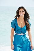 A young woman on a beach wearing a blue mini dress