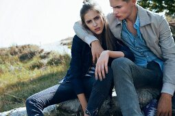 A young couple wearing casual clothing sitting on a log