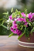 Arrangement of purple and white sweet peas, poppy seed heads and ivy in pot with patterned trim