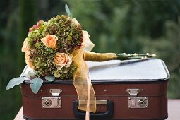 Festive bouquet of apricot roses and hydrangeas tied with ribbon on top of vintage suitcase