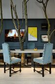 Chairs with black carved wooden frames and pale blue upholstery around table with integrated tree trunks
