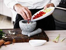 A man placing chilli and lemongrass rings into a stone mortar for crushing