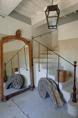 Rustikaler Treppenraum, neben gemauerter und gewendelter Treppe alter Standspiegel und schneckenförmiges Vintage Architekturelement aus Holz
