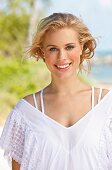 A young blonde woman on a beach wearing a white lace blouse