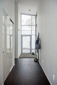 High-ceilinged narrow hallway with black-tiled floor, fitted cupboards with white sliding doors to one side and glazed house entrance at far end