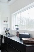 Kitchen counter with stainless steel worksurface below window with garden view