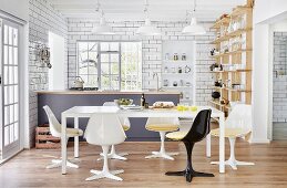 Retro shell chairs around white table in open-plan kitchen with counter and white-tiled walls