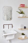 Sink with vintage wall-mounted taps below mirror and next to simple floating wooden shelves