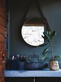 Concrete washstand with stone basin below round mirror on petrol-blue wall