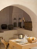 Small, simple dining area in front of arch with old, rustic vessels an candles on masonry steps and platforms