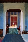 Bett vor Durchgang mit weißem, geschnitztem Holzrahmen und Blick auf Tisch in mediterranem Salon mit historischem Flair