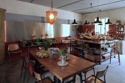 Spacious kitchen with vintage-style dining area, island counter below pendant lamps and long table below stainless steel wall cladding