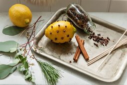 Mit Nelken gespickte Zitrone, offenes Glas mit Gewürznelken und Zimtstangen auf Vintage Tablett