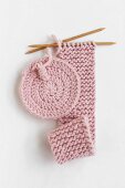 Round crocheted coaster and long piece of knitting in pink yarn