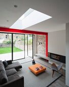 Grey couch, designer armchair and low orange coffee table in modern interior with skylight