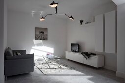 Dreiarmige Designerleuchte in weißem minimalistischem Wohnzimmer mit Licht- und Schattenspiel